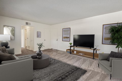A living room with a grey sofa, a grey rug, a grey coffee table, a flat screen TV, and a potted plant.
