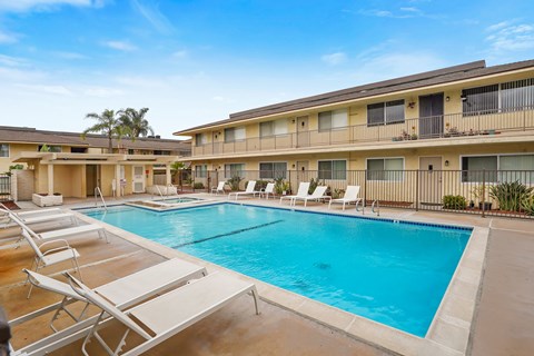 A swimming pool surrounded by sun loungers in front of apartment buildings.