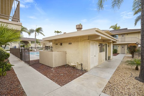 A house with a beige exterior and a brown roof is surrounded by a gravel area and a concrete walkway.