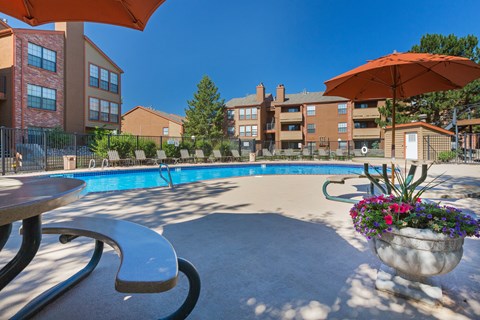 A pool area with a table and chairs and umbrellas.