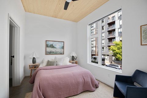 A bedroom with a pink bedspread and a painting on the wall.