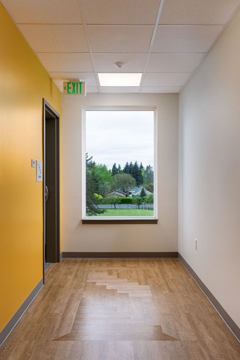 A hallway with a wooden floor and a window showing a view of trees and a house.