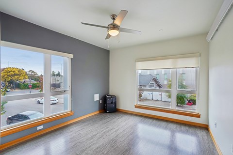 A room with a ceiling fan and a large window with a view of a street.