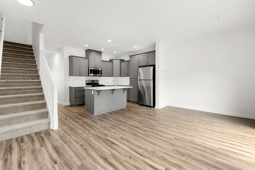 an empty living room with a kitchen with a refrigerator and a staircase