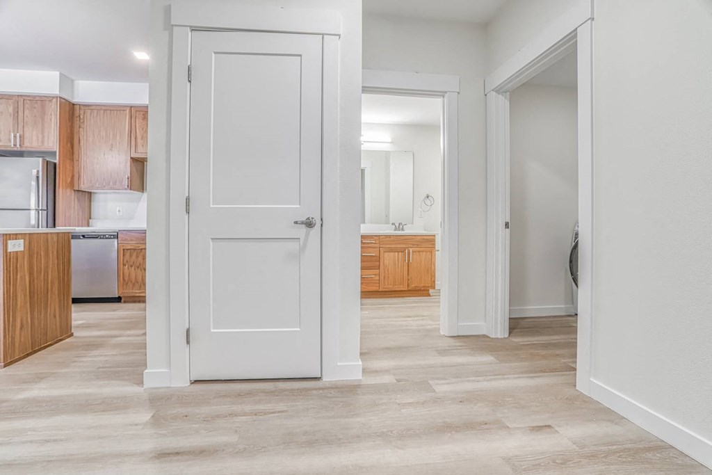 a hallway with a white door and a kitchen in the background