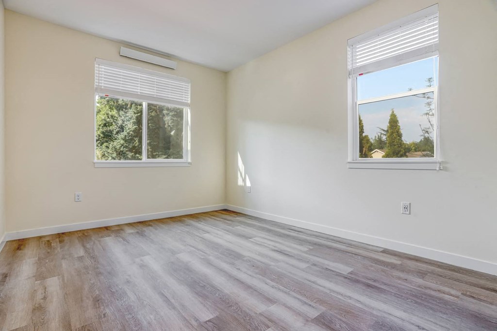 a bedroom with hardwood floors and two windows