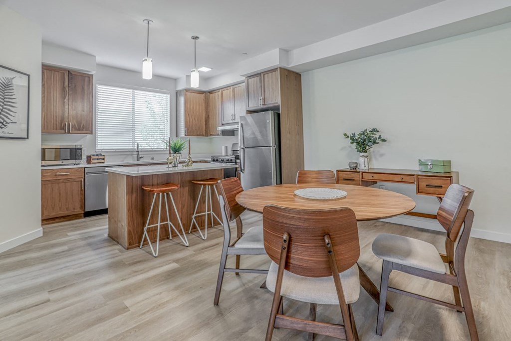 a dining area with a wooden table and chairs and a kitchen in the background