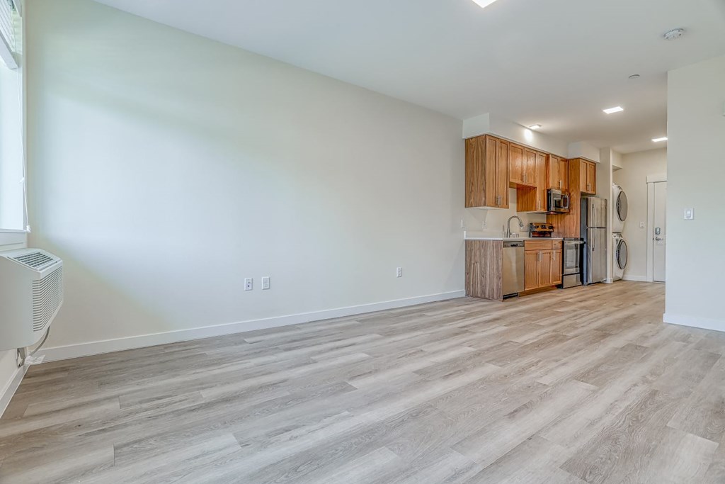 an empty living room with a kitchen in the background
