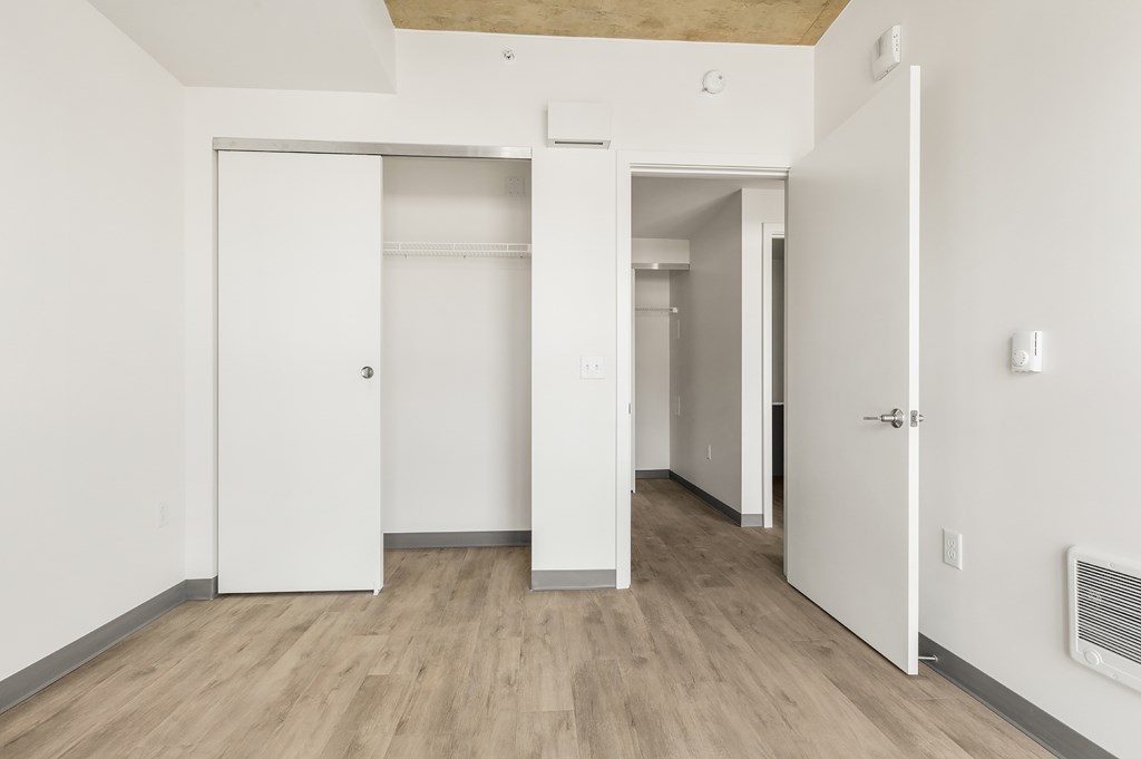 A room with white walls and wooden flooring with two open doors.
