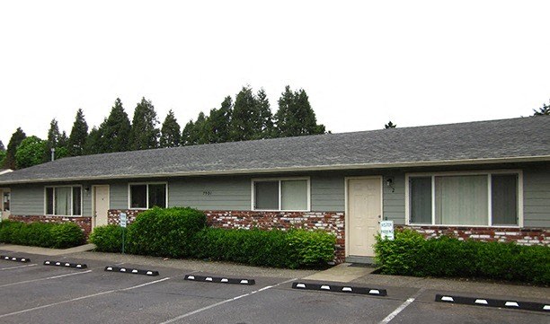 a gray house with a parking lot and bushes
