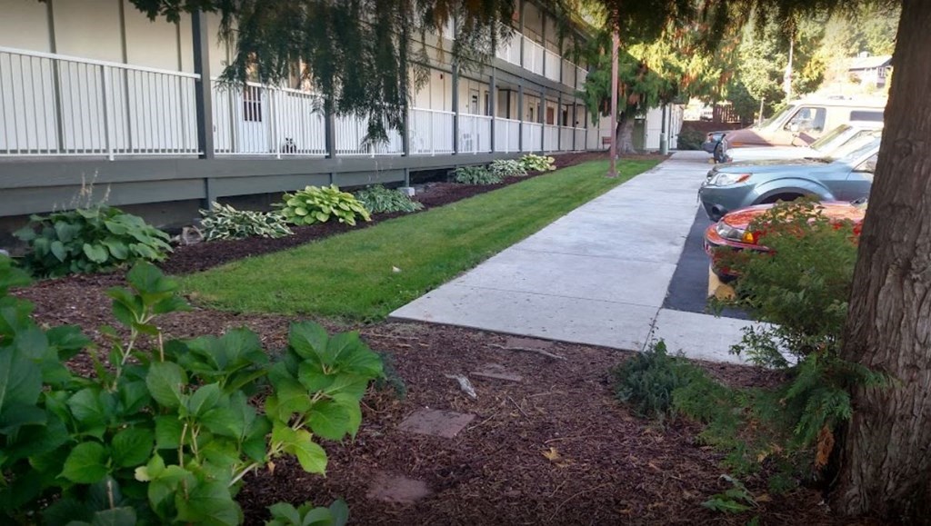 a sidewalk in front of a building with trees and plants