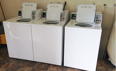 Three white front loading washing machines are lined up in a row.