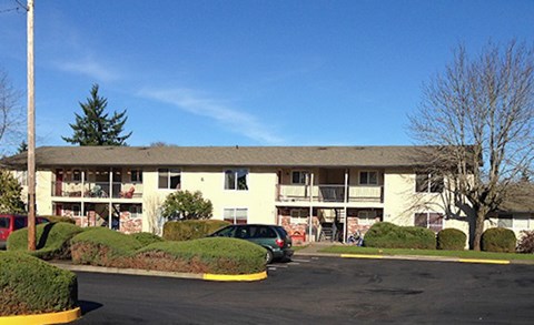 Apartment complex with a green hedge and a car parked in front.