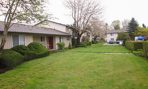 A grassy area in front of a building with a tree and bushes.