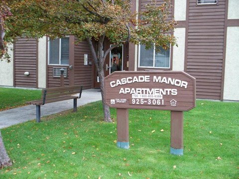 a wooden sign in the grass in front of a building