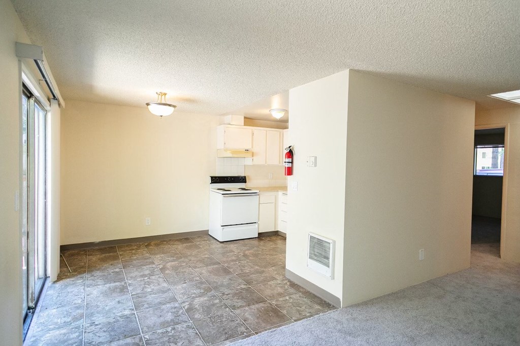 an empty living room with a kitchen in the background