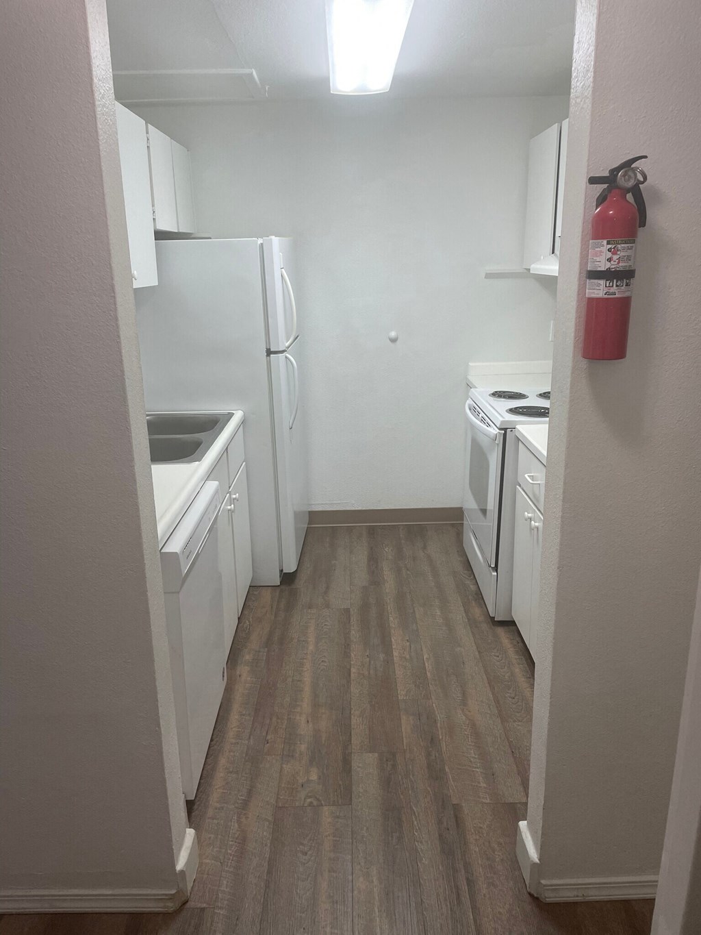 a kitchen with white appliances and a fire extinguisher on the wall