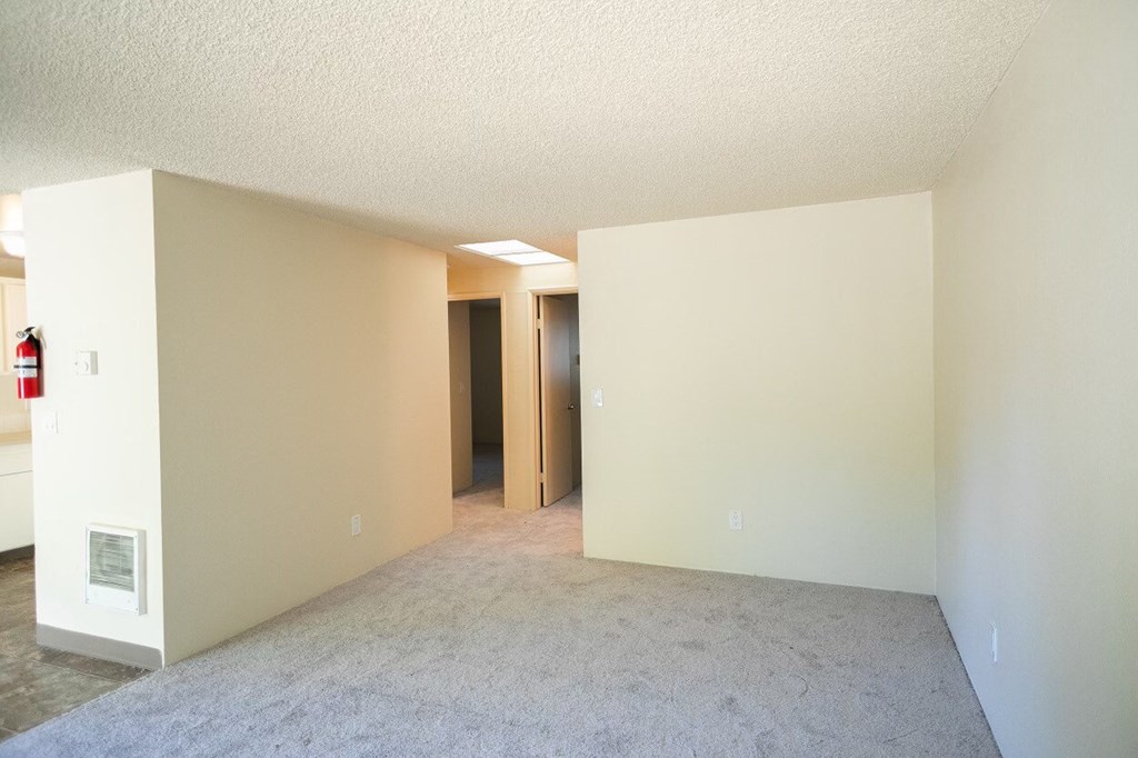 an empty living room with a kitchen in the background
