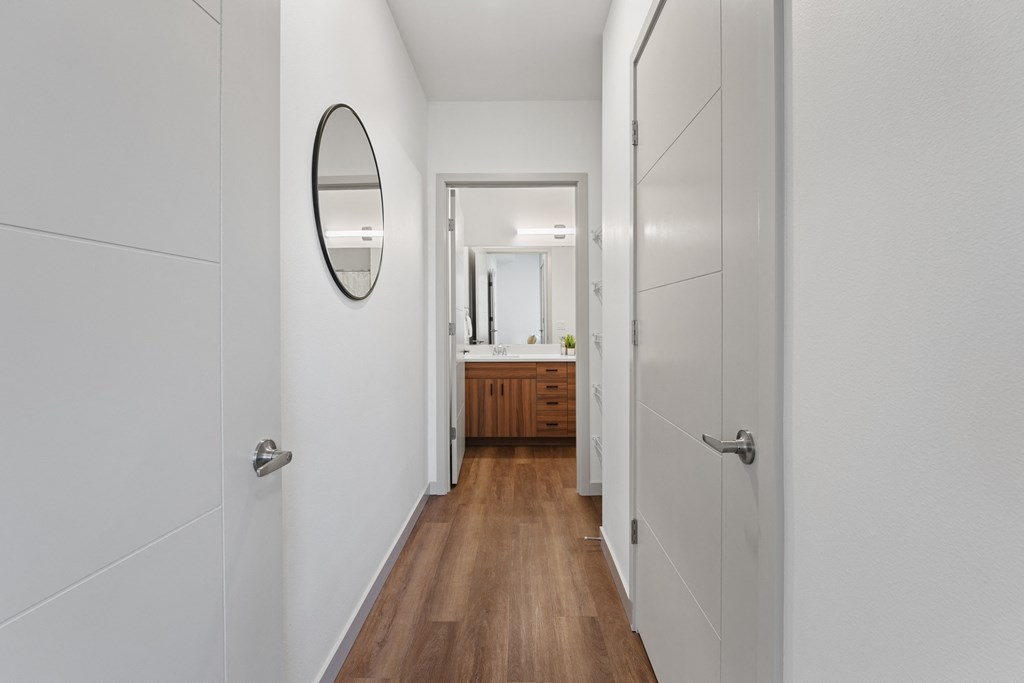a hallway with white walls and wooden floors and a mirror
