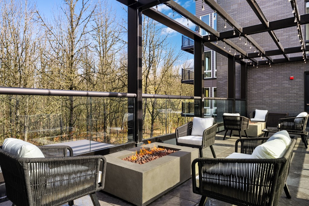 a covered patio with chairs and table and a fire pit over looking the forest