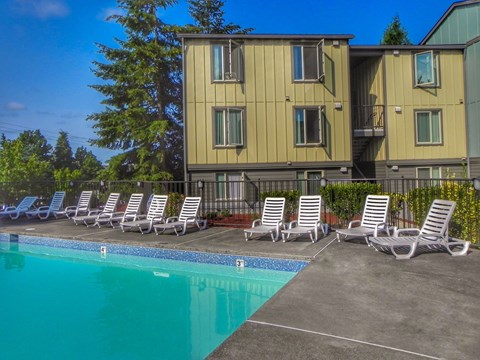 A pool with chairs and a building in the background.