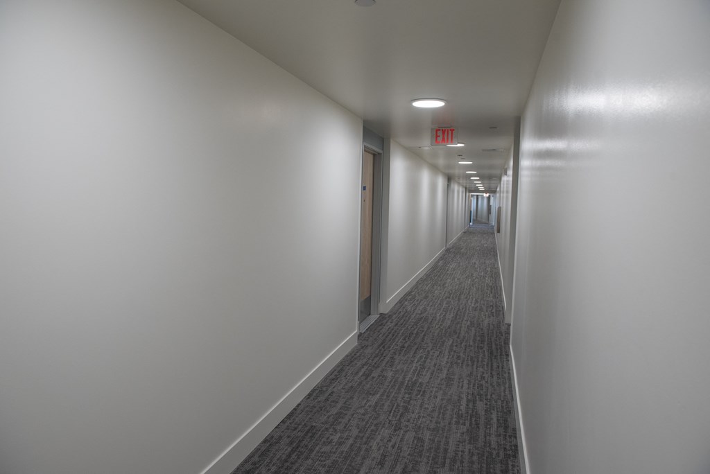 a long corridor in a building with white walls and a red exit sign