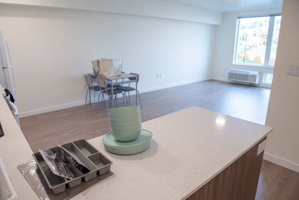 an empty living room with a kitchen counter with a stack of plates on it