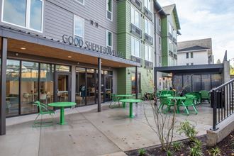 a patio with green tables and chairs outside of a building