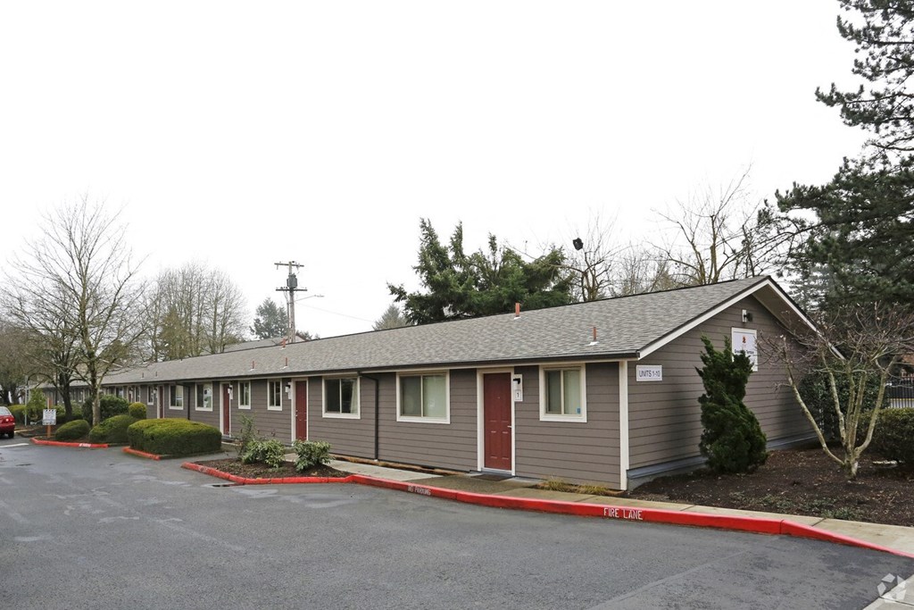 A building with grey walls and red doors is surrounded by a parking lot.