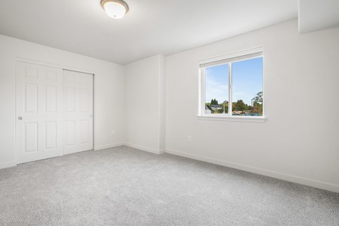 A room with a white door and a window showing a view of trees and a house.
