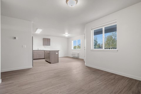 A spacious room with wooden flooring and a kitchen area in the background.