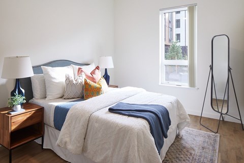 A bed with a white comforter and a blue blanket is in the center of the room.