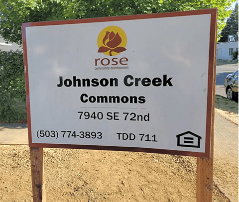 A sign for Johnson Creek Commons is displayed on a wooden post.