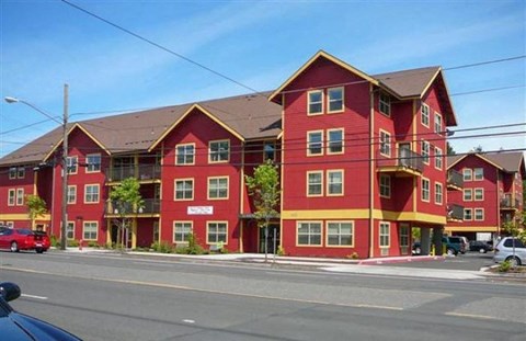 A red and yellow apartment building with a car parked in front.
