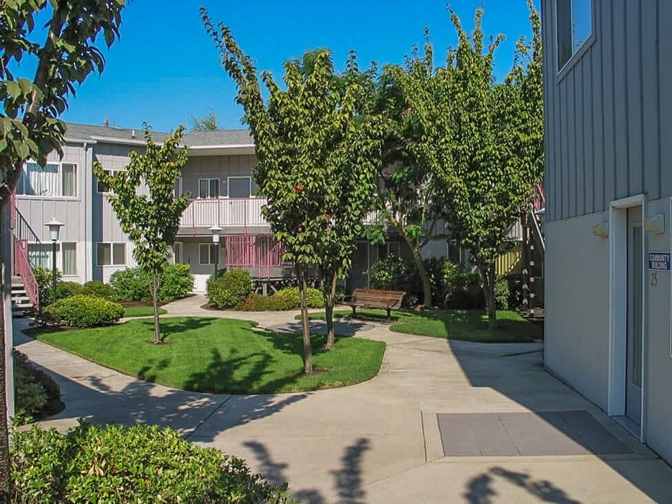 a courtyard with benches and trees in front of an apartment building
