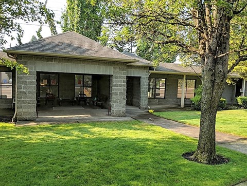 A small stone building with a porch and a tree in front.