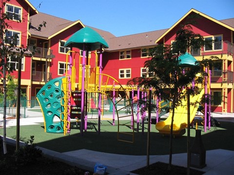 A playground with a yellow slide and a green umbrella.