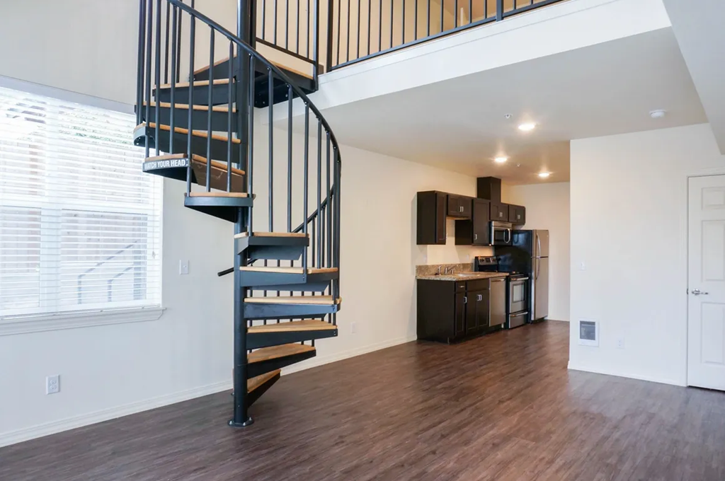a spiral staircase leads up to a loft in a home with a kitchen in the background