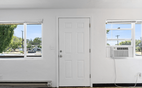 A white door is in a room with a window and an air conditioner.