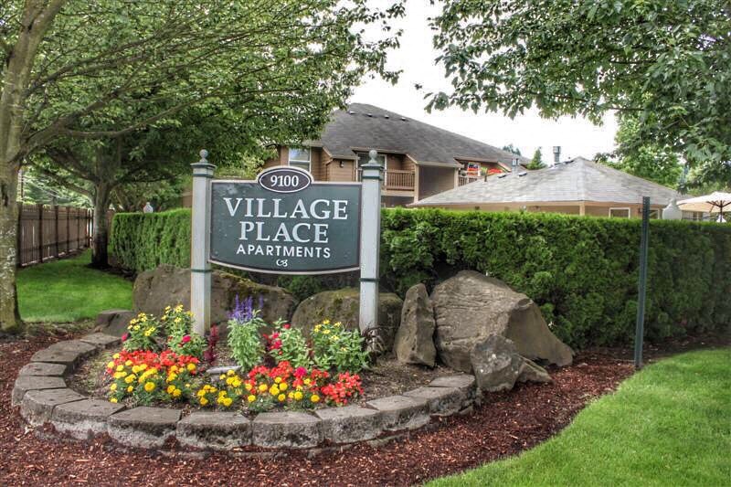 a village place apartments sign in front of a garden and rocks
