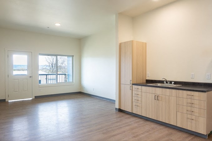 an empty living room with a kitchen and a door to a balcony