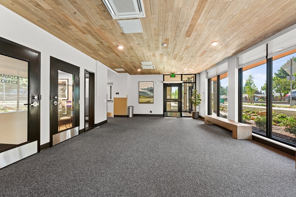 A hallway with a wooden ceiling and carpeted floor leading to a door with a glass panel.