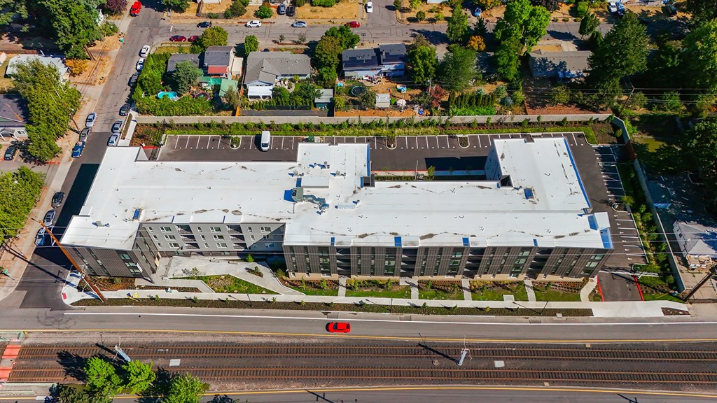 A large building with a flat roof is surrounded by trees and a parking lot.