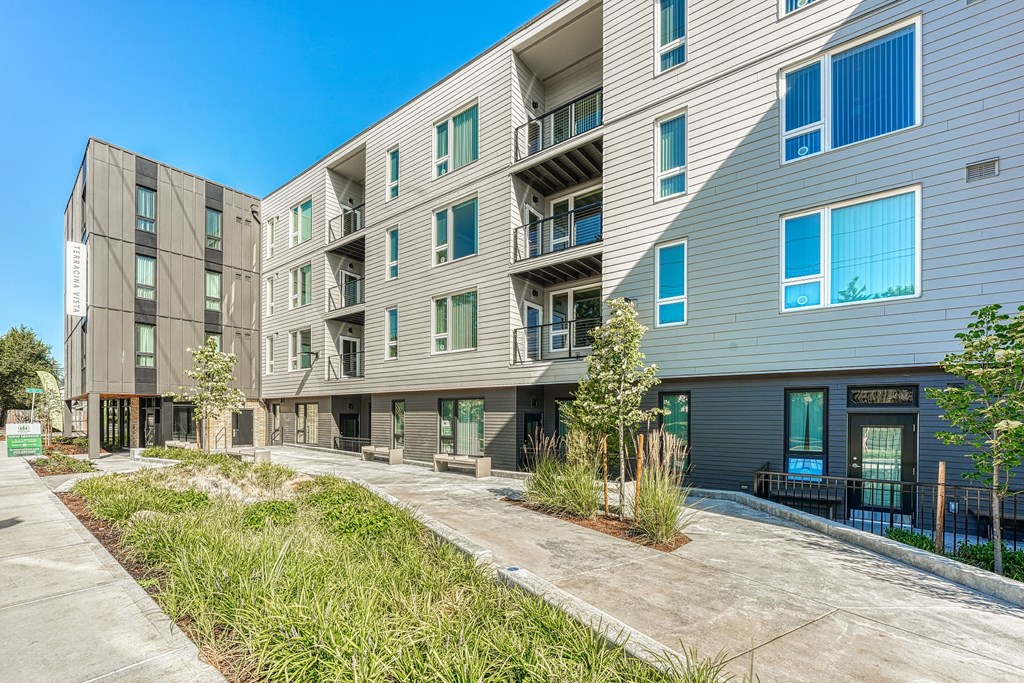 A modern apartment complex with balconies and greenery in front.