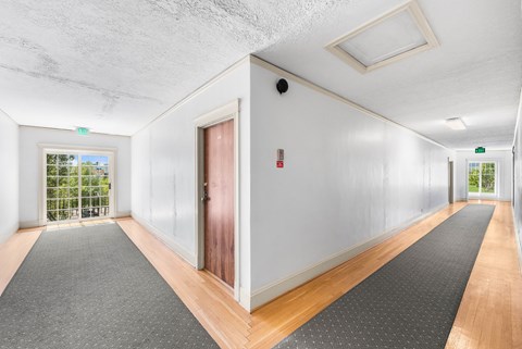 A long hallway with a red door and a window with a view of trees.