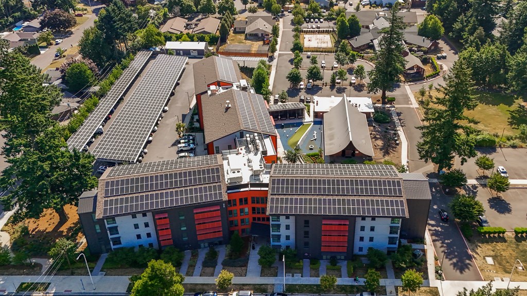 A modern building with a red and white facade is surrounded by trees and other buildings.