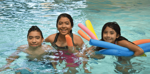 Three girls are in a pool with pool noodles.