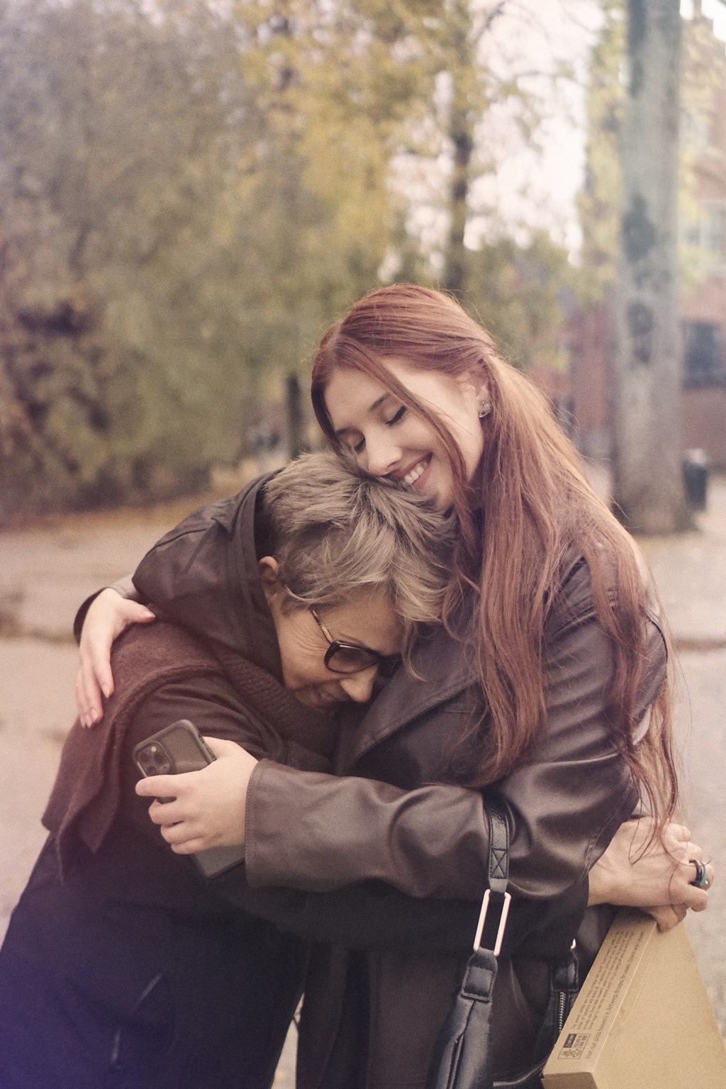 a girl hugging another girl while looking at a cell phone
