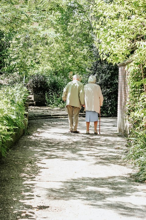an elderly couple walking down a garden path