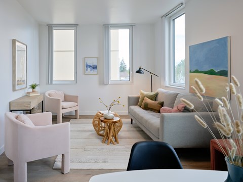 A living room with a grey couch, a pink chair, and a painting on the wall.